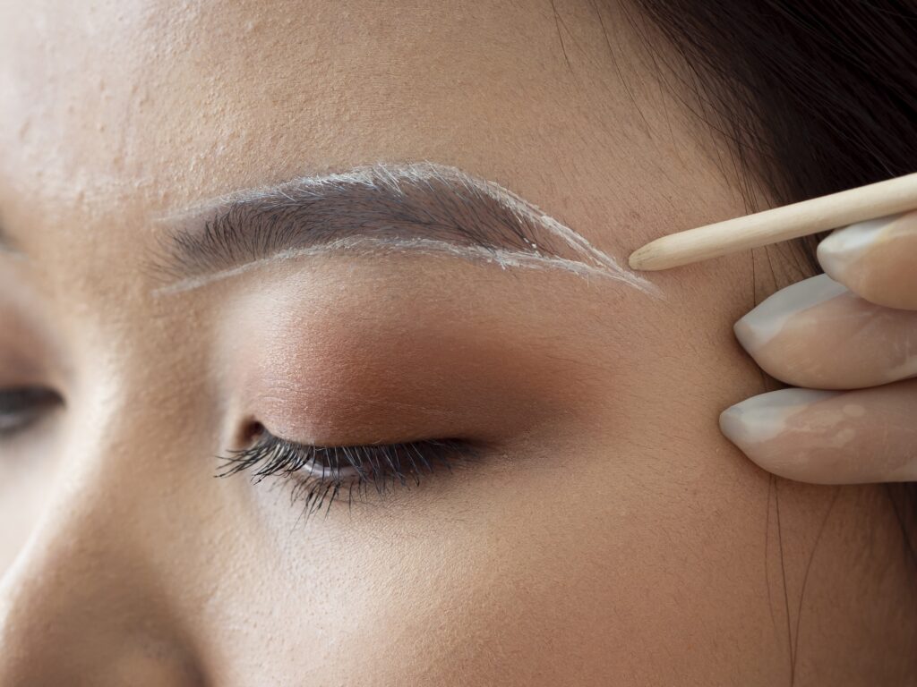 A provider's hand uses a white pencil to mark out the new brow shape for a client as she prepares for brow waxing in Georgetown.