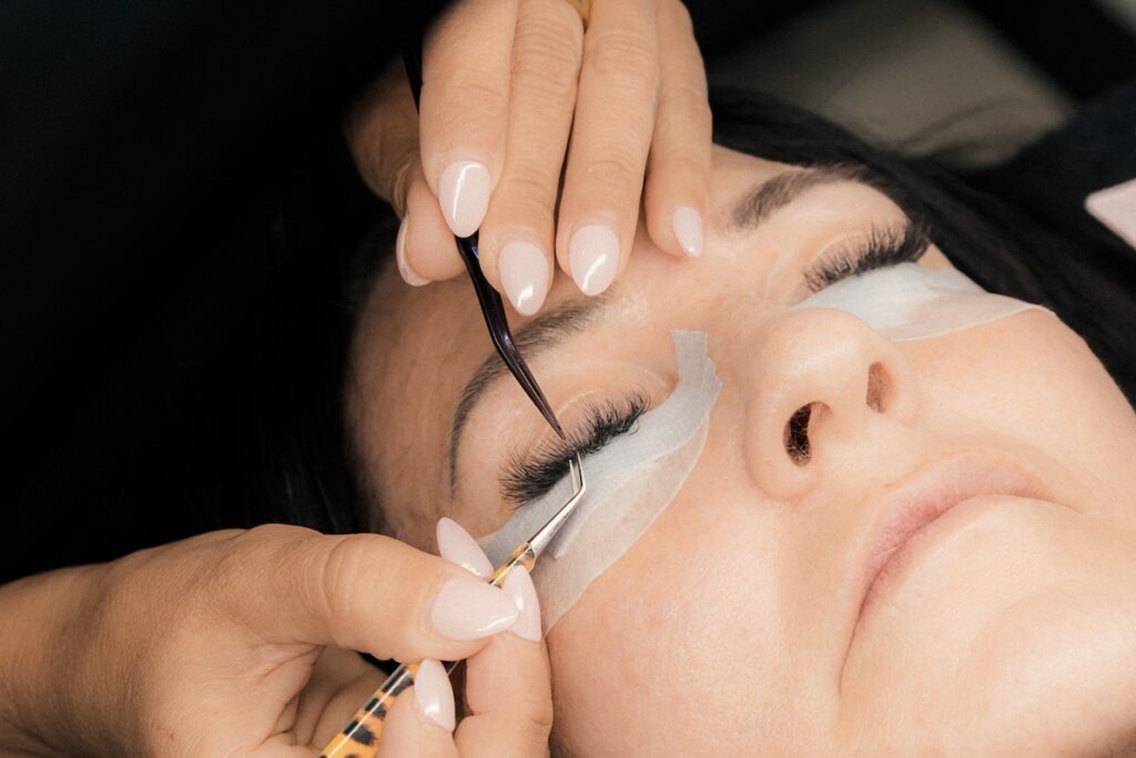 A close-up of a lash artist placing eyelash extensions on a client's lash line.